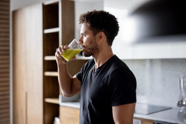 A man drinks a juice in the kitchen.