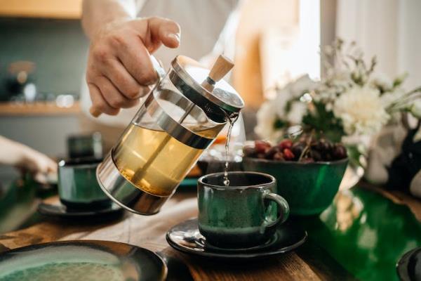A hand pours a pot of tea into a green cup.
