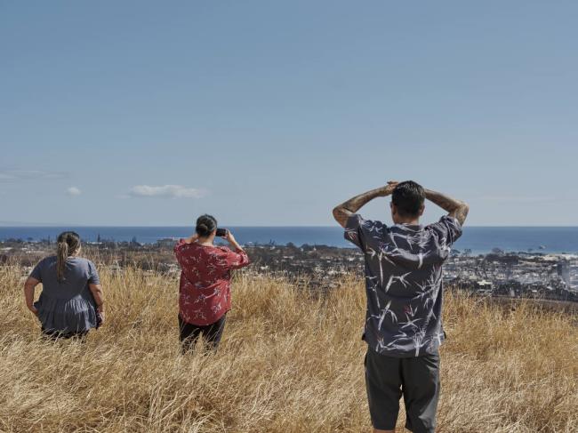 People look at the destruction of Lahaina due to wildfires in Lahaina, Hawaii, Aug. 11, 2023. A sweeping series of plantation closures in Hawaii allowed highly flammable no<em></em>nnative grasses to spread on idled lands, providing the fuel for huge blazes. (Philip Cheung/The New York Times)