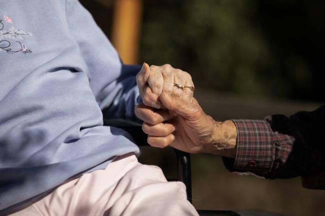 An elderly couple hold hands at nursing home in California in 2021. Photo by Anne Wernikoff, CalMatters